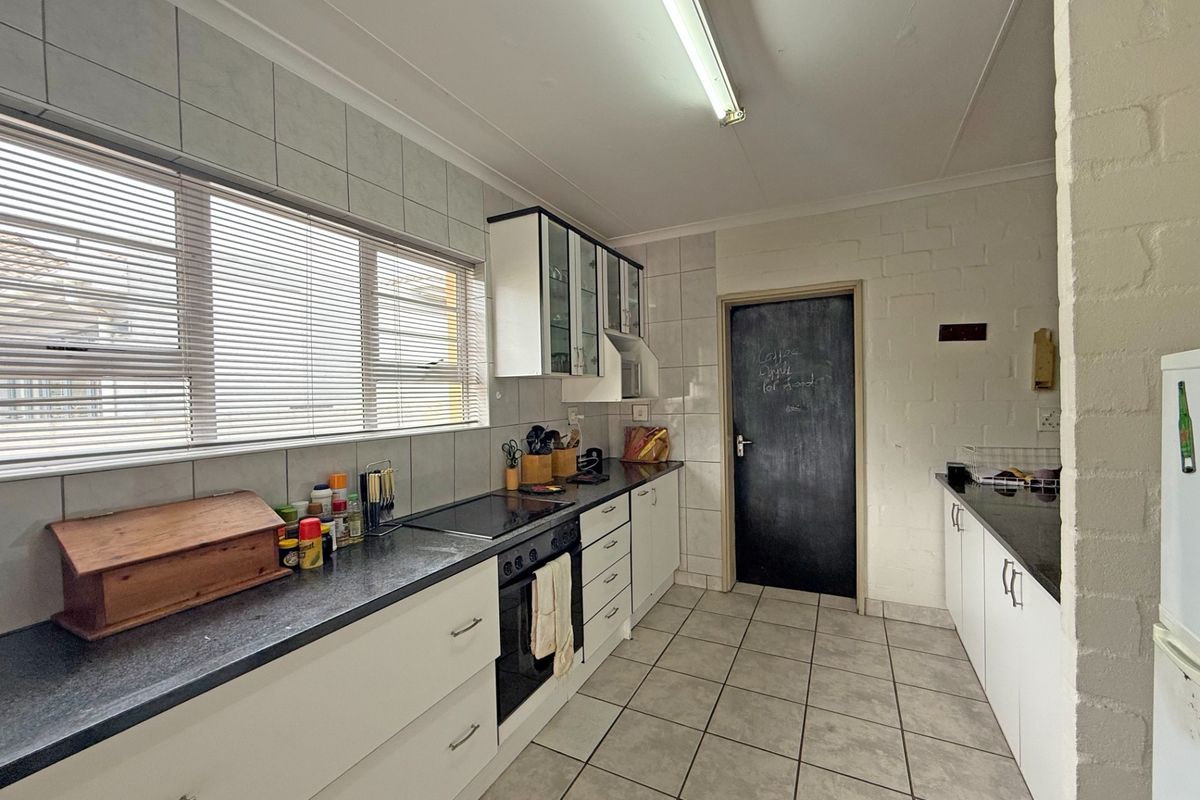 A functional kitchen featuring white cabinetry, dark countertops, tiled splashbacks, and tiled flooring, providing a practical workspace with ample storage.