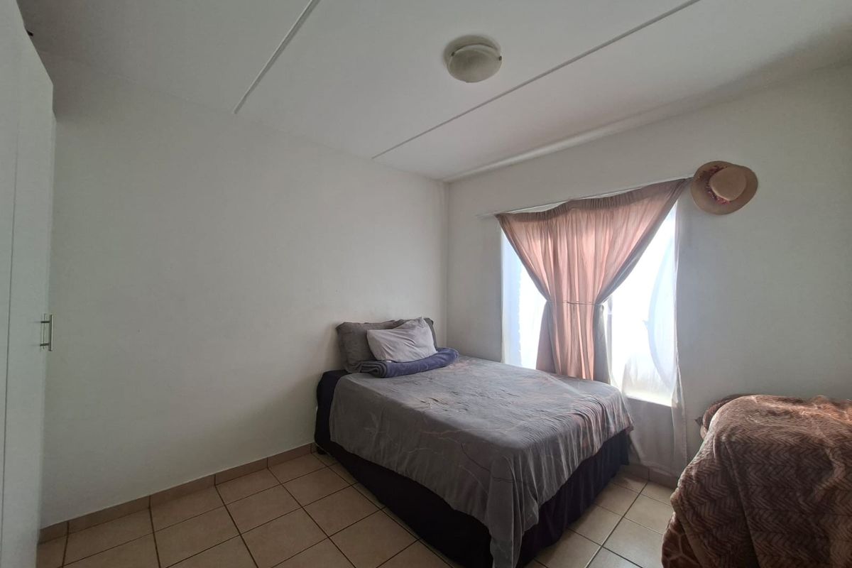 A functional bedroom featuring tiled flooring, a built-in wardrobe, and a window with curtain treatments.