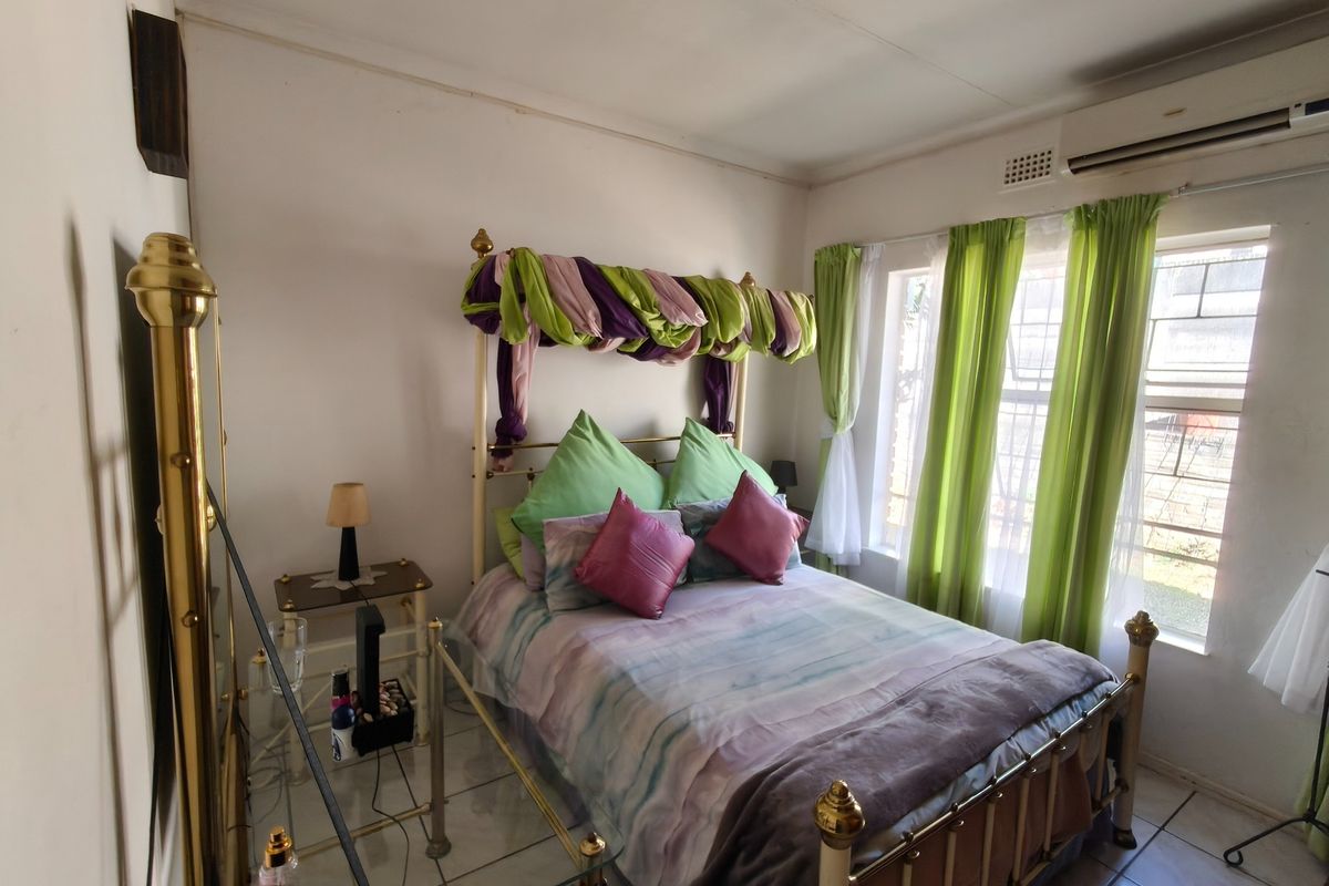 A bedroom featuring tiled flooring, a wall-mounted air conditioning unit, and large windows allowing for natural light.
