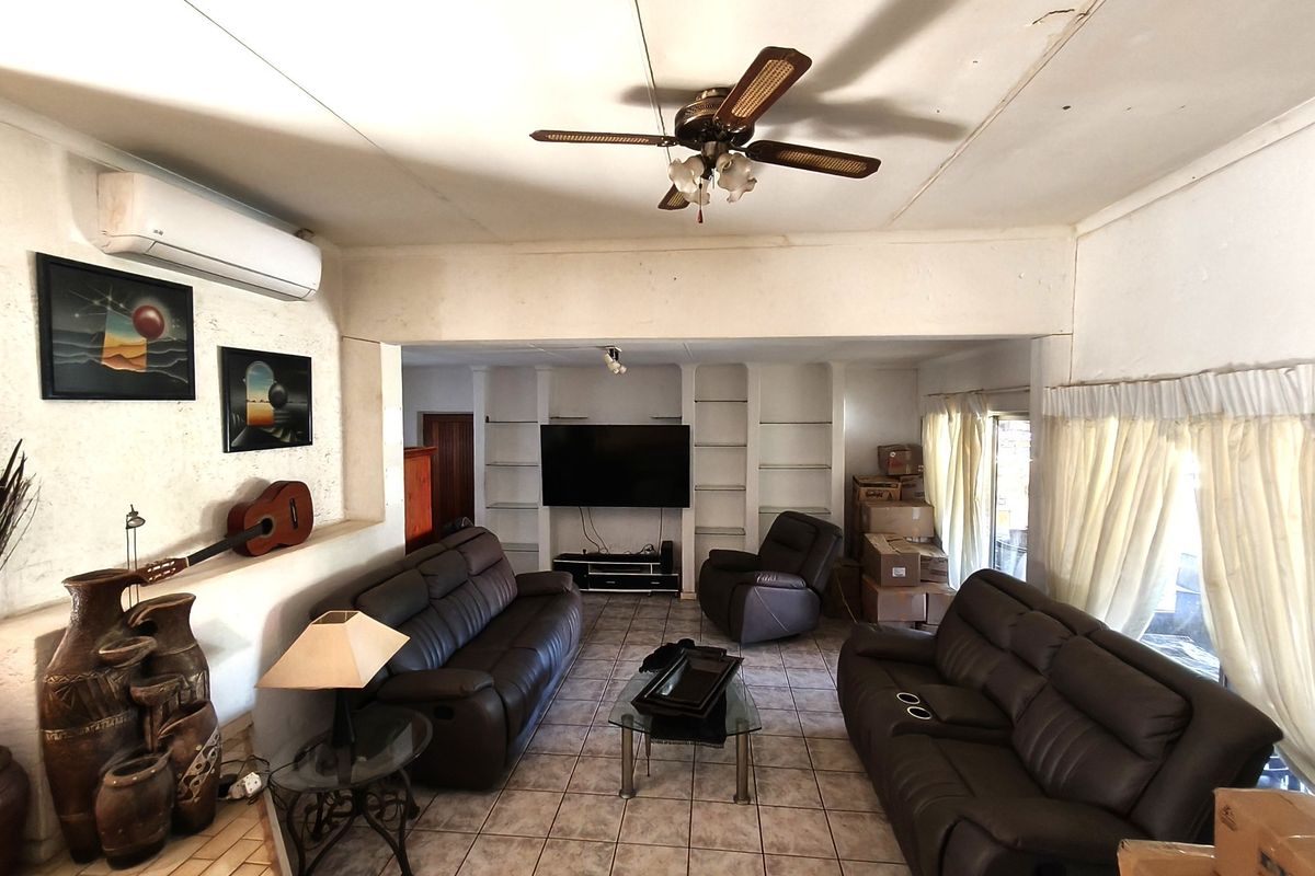 Spacious living room featuring tiled flooring, built-in shelving units, a ceiling fan, and a wall-mounted air conditioning unit.