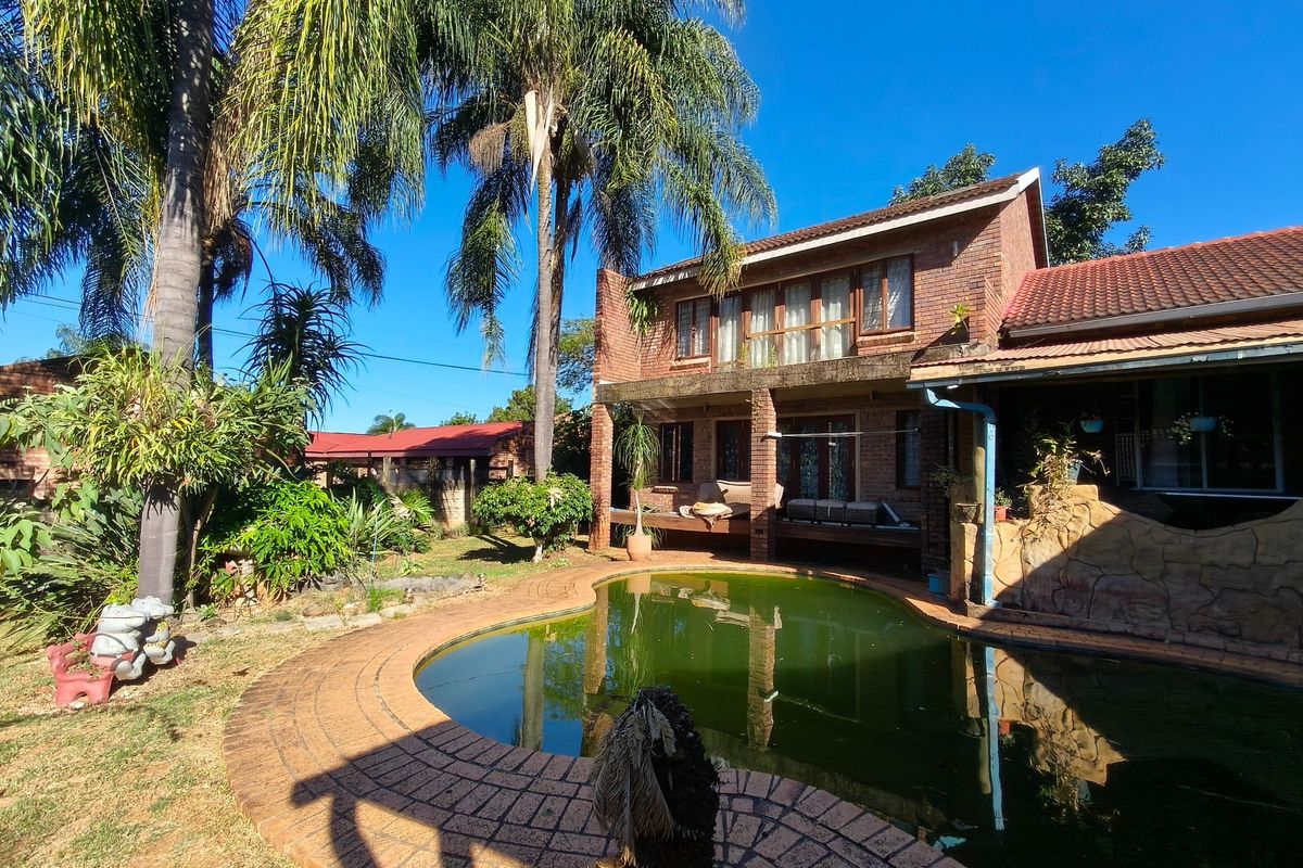 Rear view of a double-story brick house featuring a swimming pool, covered patio area, and established garden surroundings.