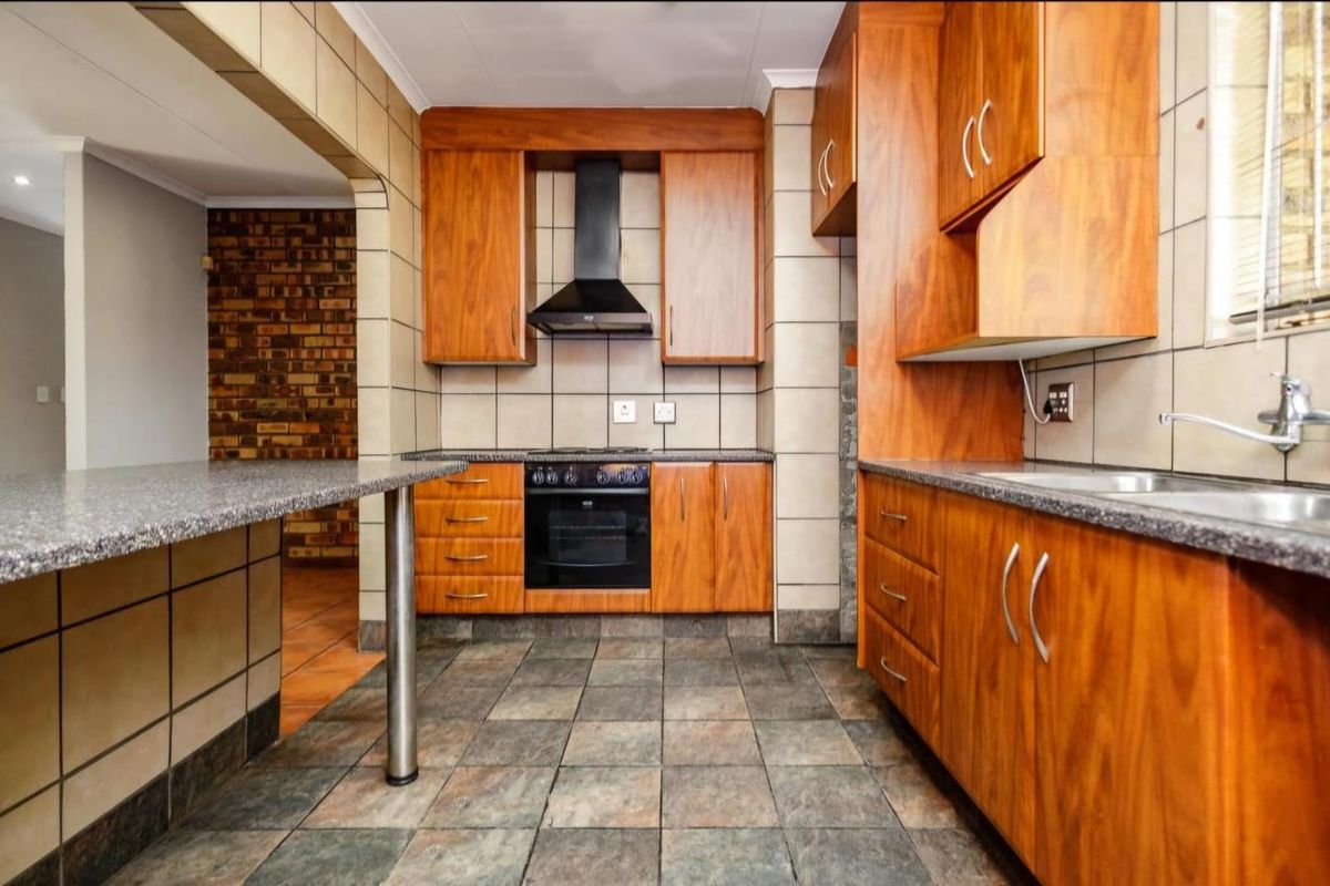 A functional kitchen featuring wood-finish cabinetry, granite-look countertops, a built-in oven with extractor fan, and tiled flooring throughout.