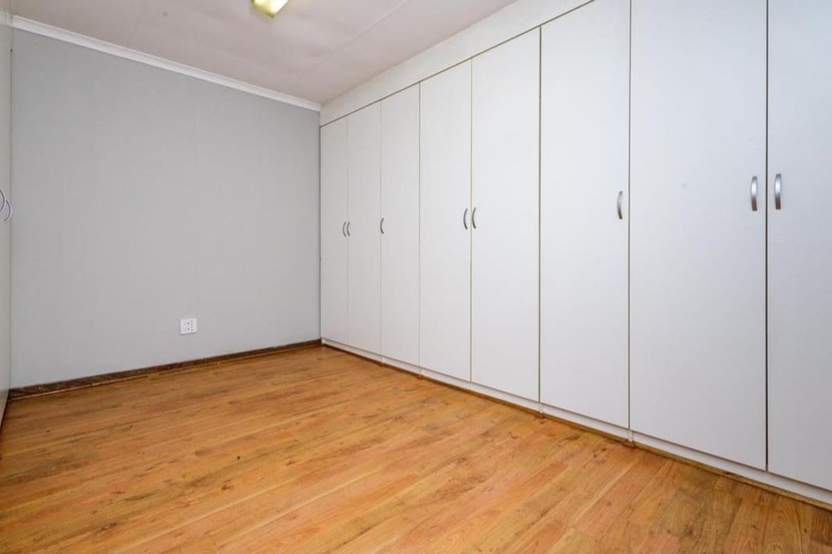 A clean, empty bedroom featuring extensive floor-to-ceiling built-in cabinetry and wood-look laminate flooring.
