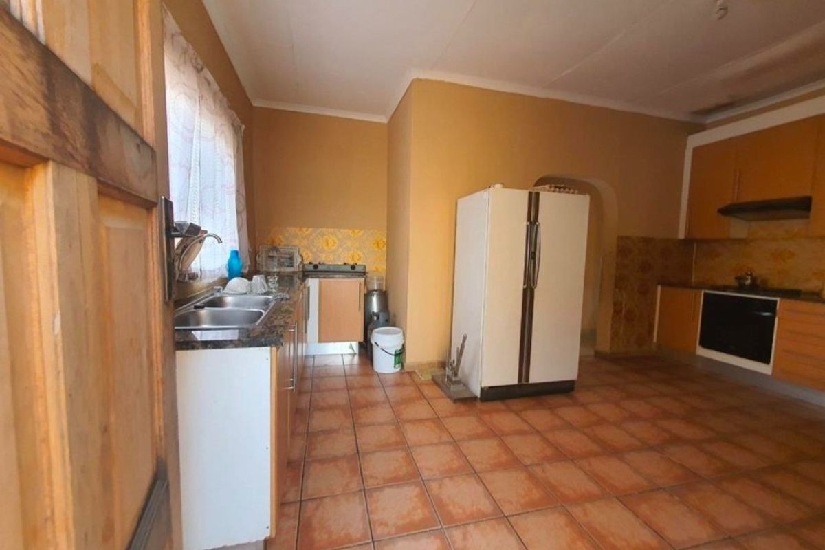 A dated kitchen featuring wooden cabinetry, tiled flooring, and built-in oven and hob, offering potential for a modern renovation.