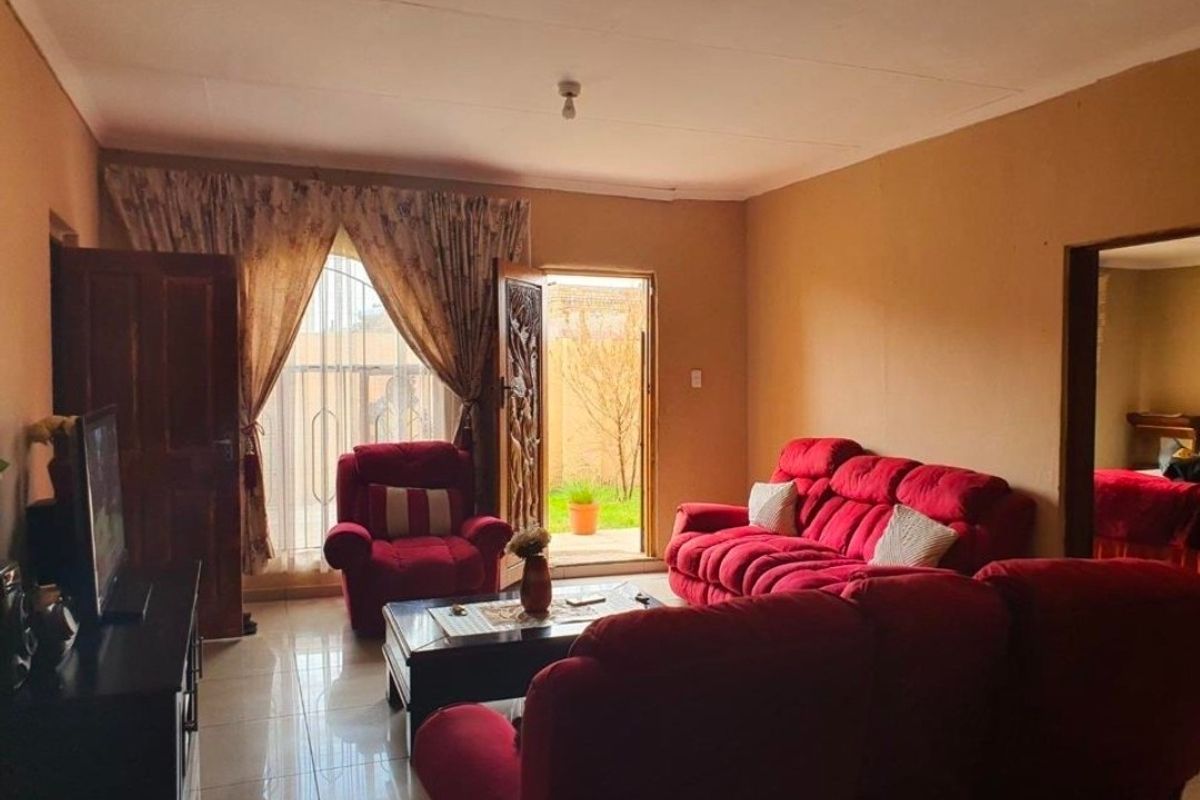 A living room featuring tiled flooring, a wooden door leading to the exterior, and a large window with curtains.
