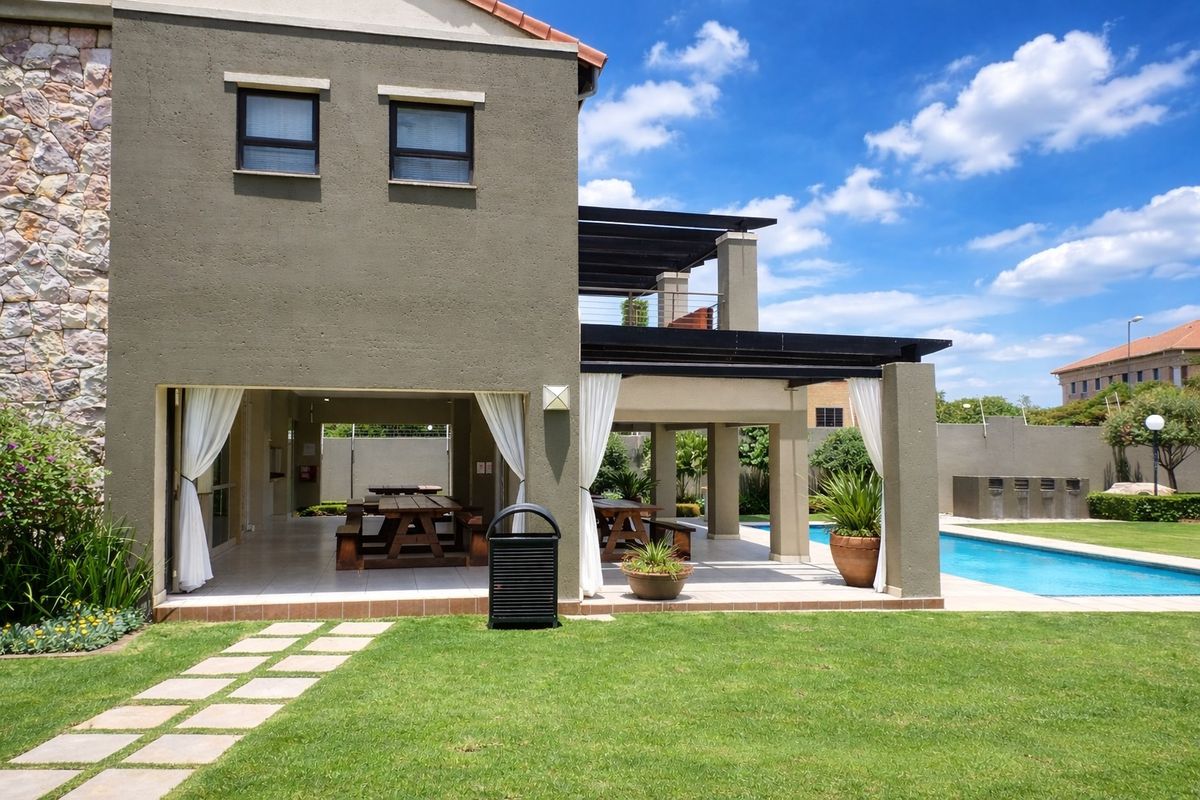 A spacious covered patio area overlooking a swimming pool and landscaped garden, featuring tiled flooring and a modern pergola structure.