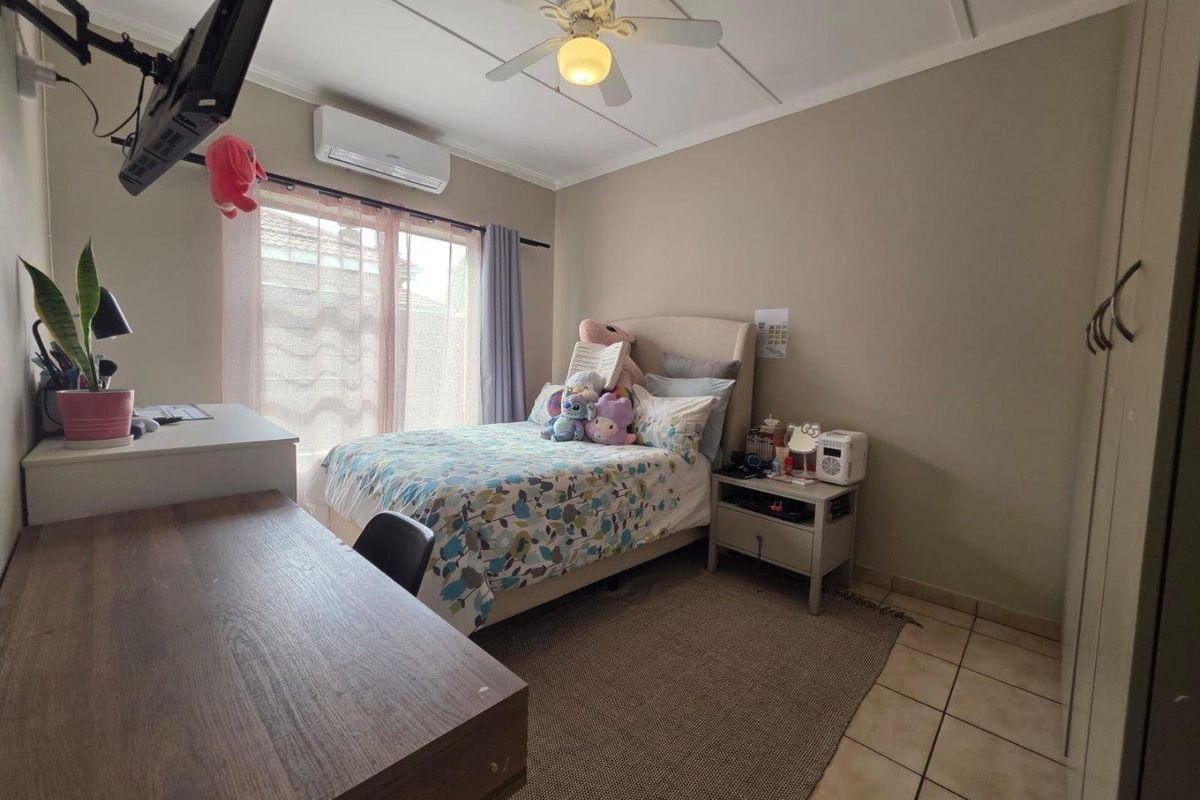 A functional bedroom featuring tiled flooring, a ceiling fan, and a wall-mounted air conditioning unit.