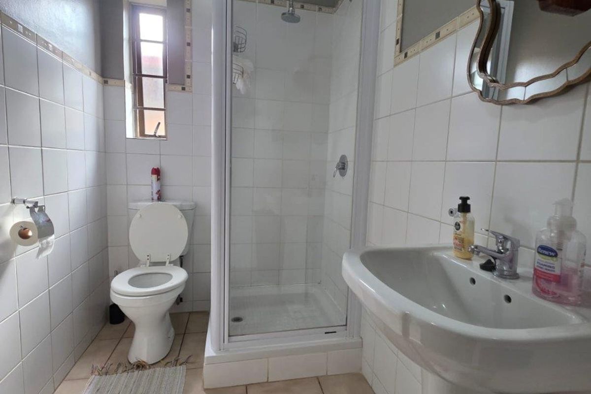 A functional bathroom featuring a pedestal basin, a glass-enclosed shower, and a toilet, finished with neutral wall and floor tiling.