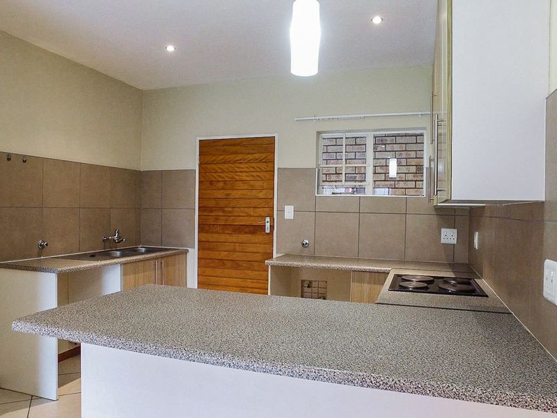 A clean, functional kitchen featuring granite countertops, a built-in electric hob, stainless steel sink, and ample cabinetry with neutral tiled backsplash.