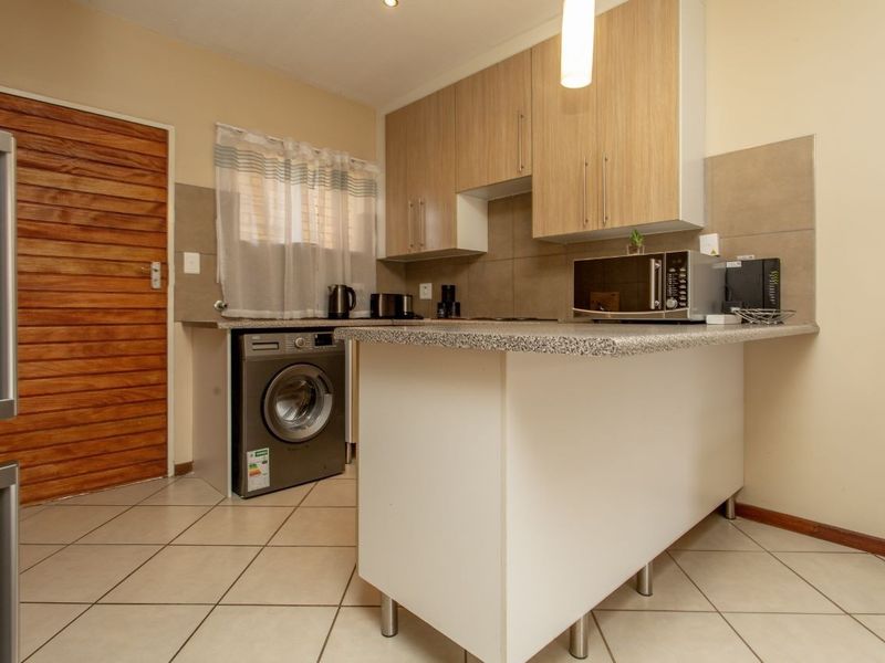 Compact kitchen featuring laminate cabinetry, granite countertops, tiled backsplash, and a functional breakfast bar, with tiled flooring throughout.