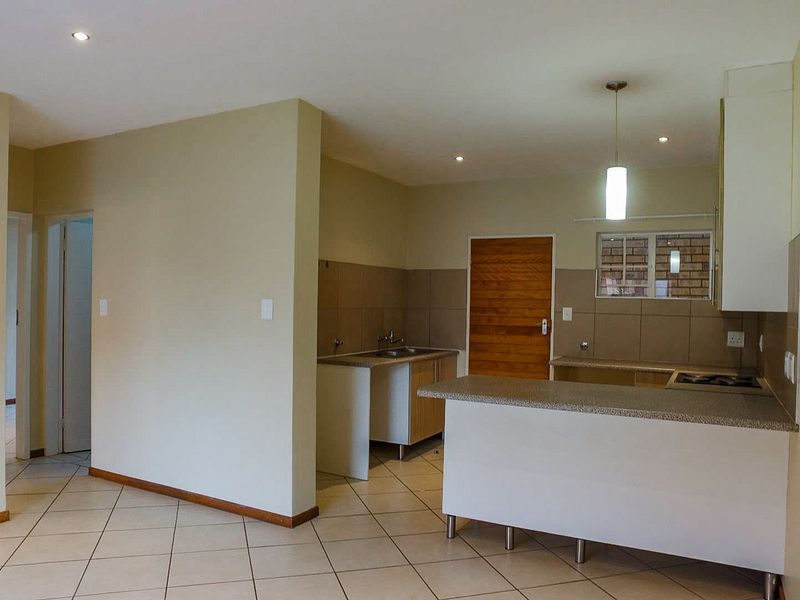 Open-plan kitchen area featuring tiled flooring, built-in cabinetry, a breakfast counter, and integrated hob, offering a functional and clean layout.