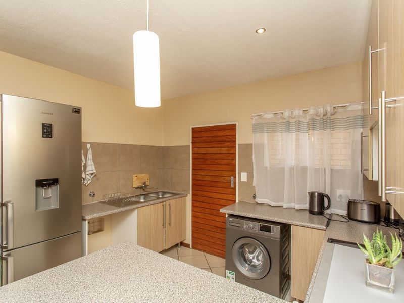 Functional kitchen featuring laminate cabinetry, granite-look countertops, a stainless steel double sink, tiled backsplash, and tiled flooring.