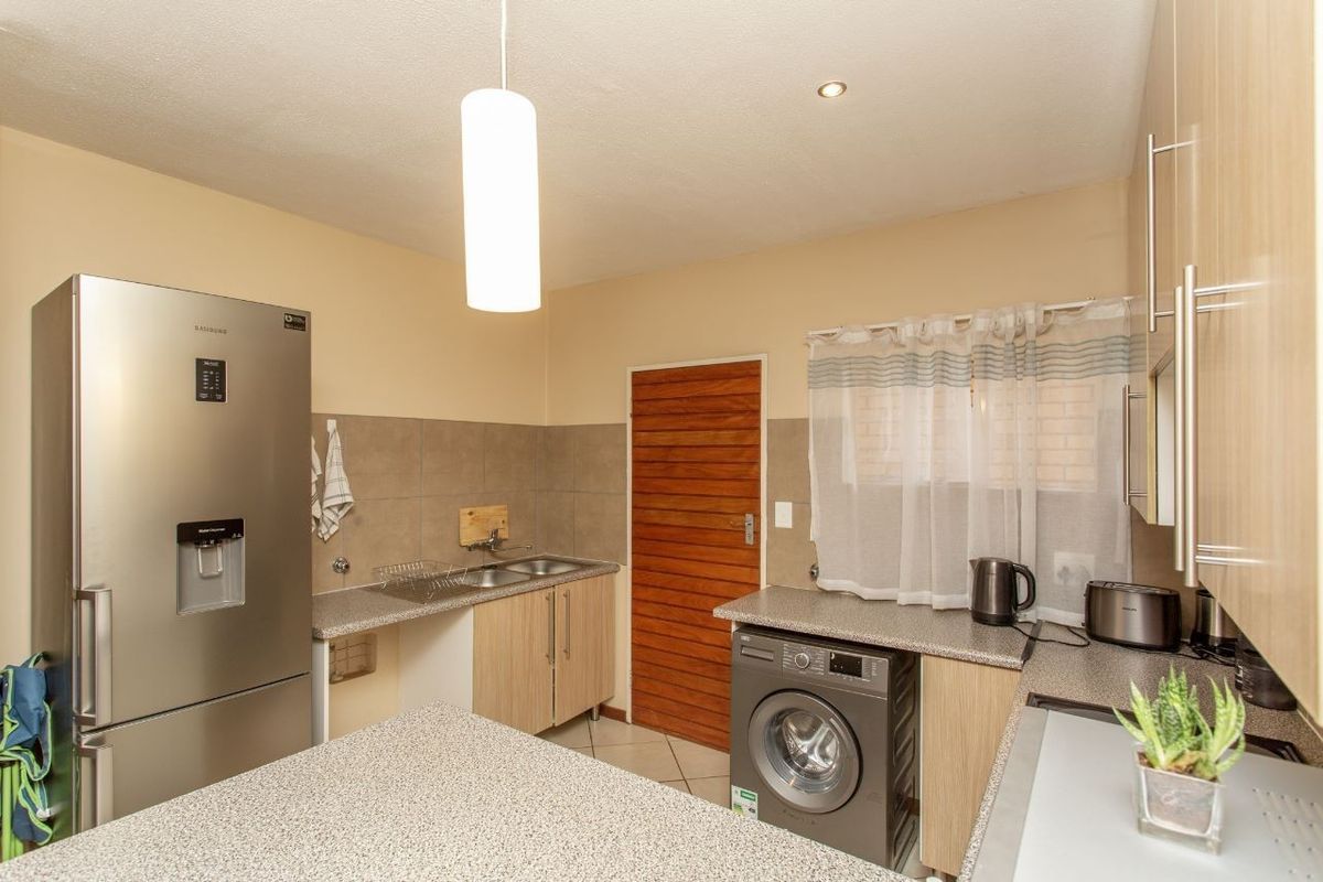 Functional kitchen featuring laminate cabinetry, granite-look countertops, a stainless steel double sink, tiled backsplash, and tiled flooring.