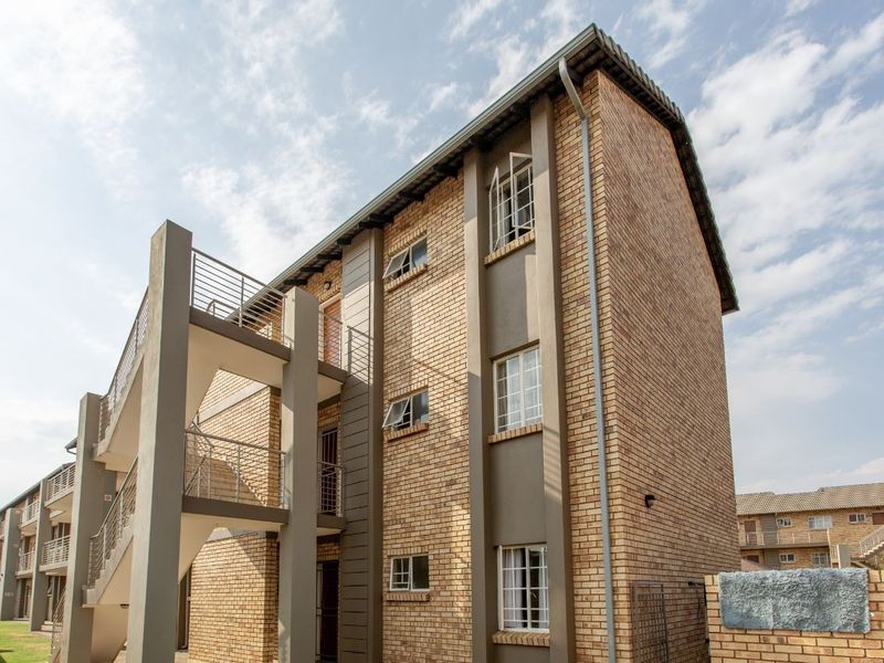 A multi-story apartment building featuring a face brick facade, external staircases with metal balustrades, and well-maintained casement windows.