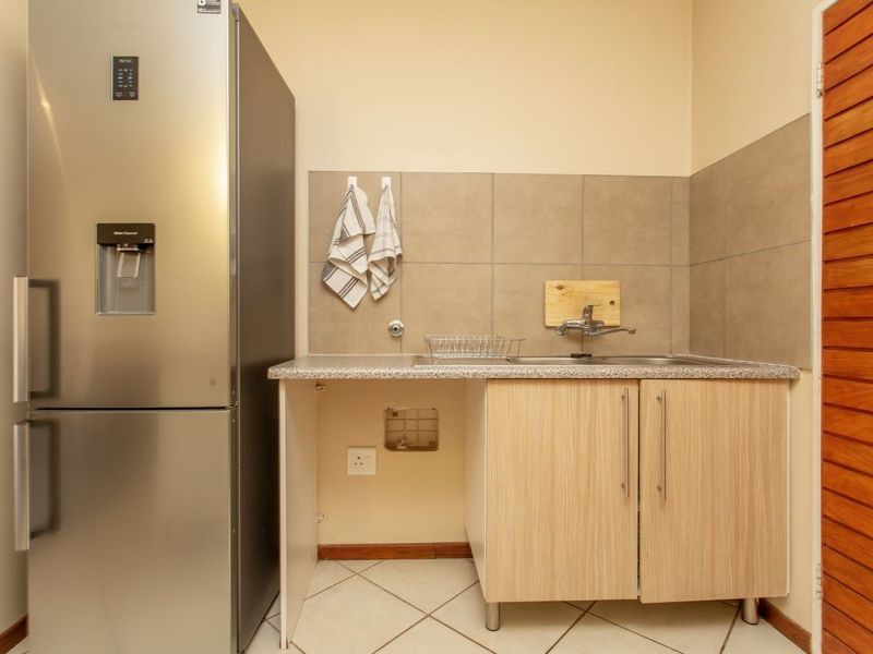 A functional scullery area featuring a stainless steel sink, tiled splashback, laminate cabinetry, and space for a refrigerator.