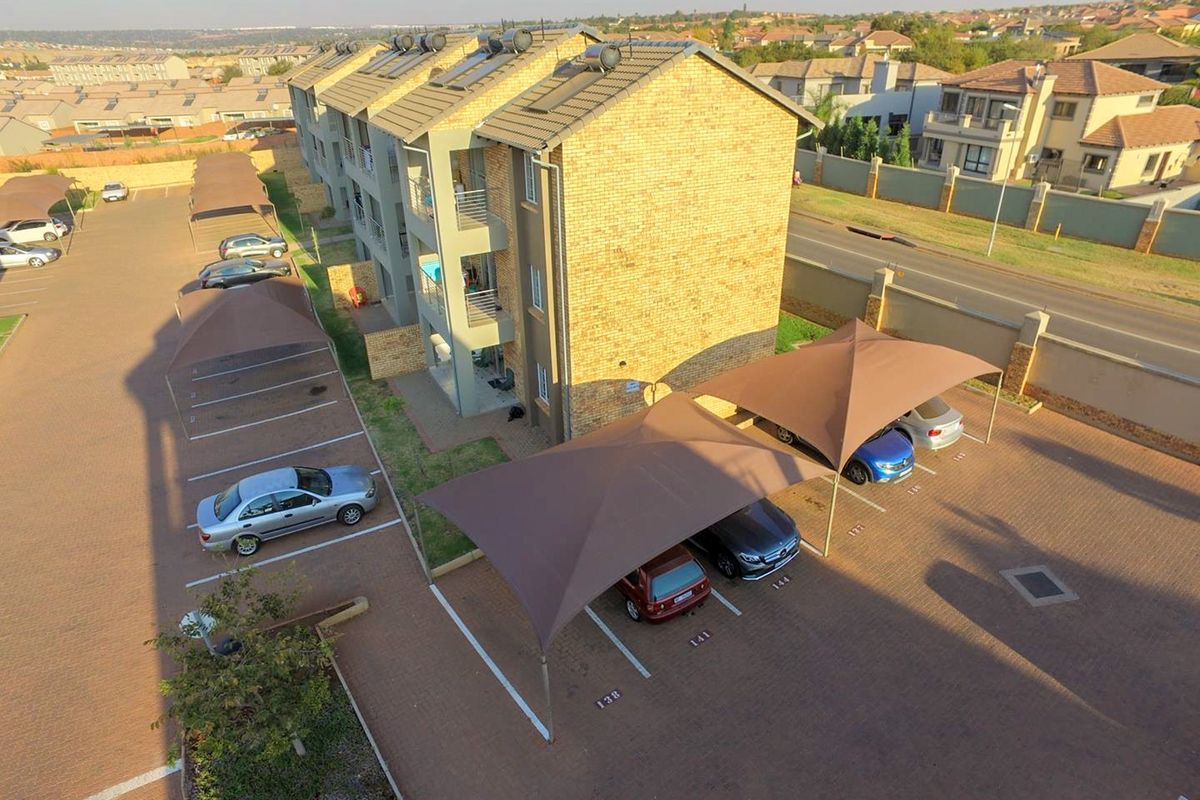 Aerial view of an apartment complex featuring brick construction, solar water heating systems, and designated paved parking bays with shade cloth carports.