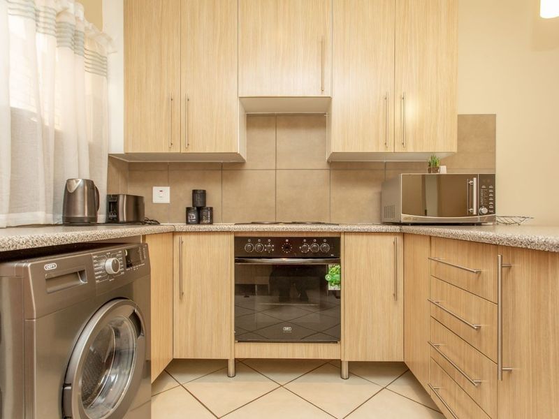 A functional kitchen featuring light wood-finish cabinetry, granite-look laminate countertops, a built-in oven with hob, and tiled flooring.