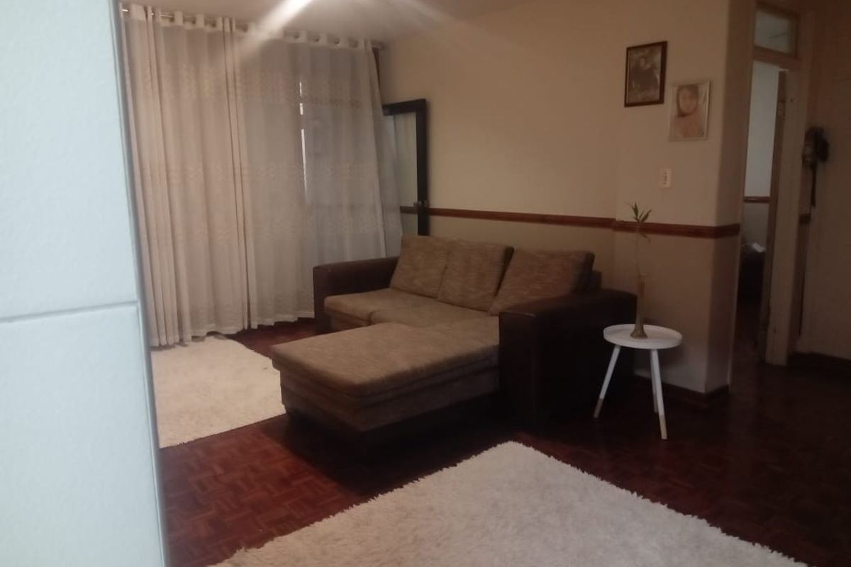 A living room featuring dark parquet flooring, a dado rail, and large windows covered by curtains, providing a comfortable and functional living space.