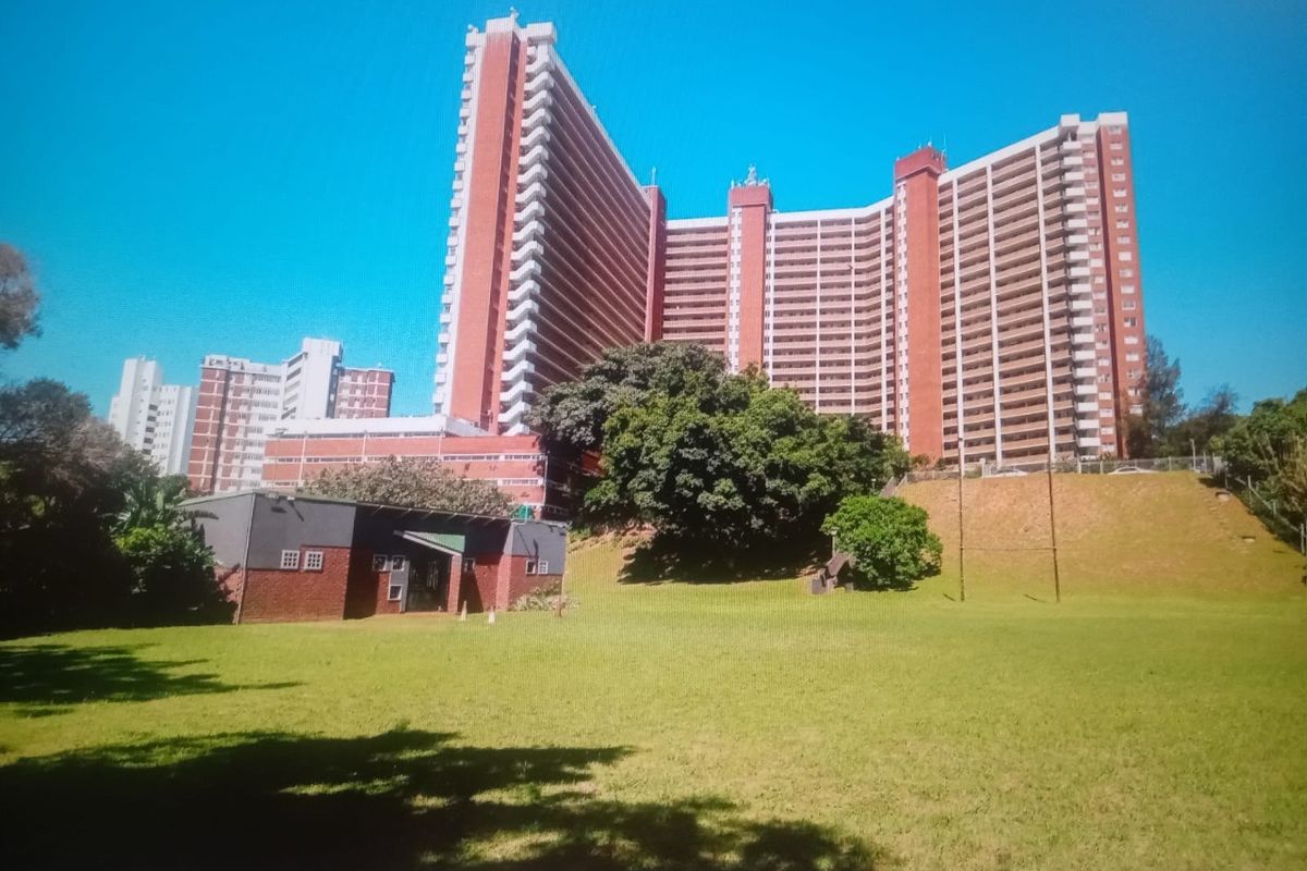 Exterior view of a large multi-story residential apartment complex featuring red brick facade and surrounding landscaped green space.