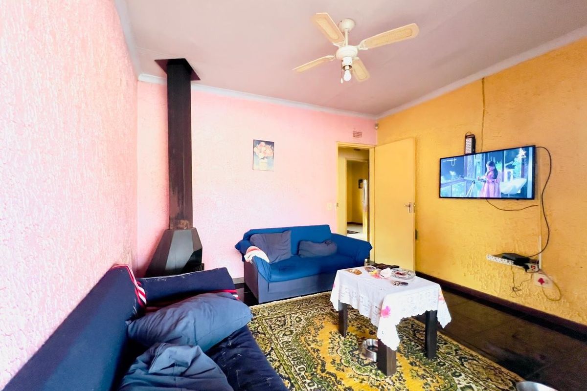 A living room featuring a built-in fireplace, ceiling fan, and tiled flooring, with vibrant wall finishes.