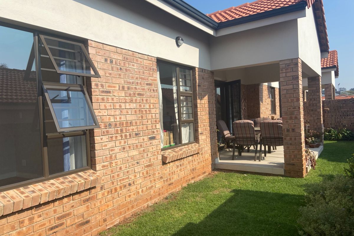 A well-maintained brick exterior featuring a covered patio area, tiled roof, and aluminium-framed windows overlooking a private garden space.
