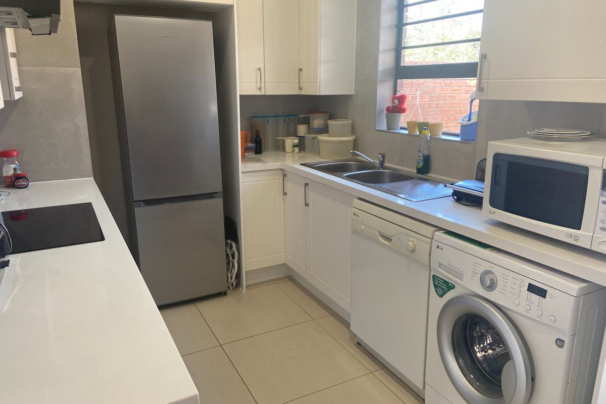 A functional kitchen featuring white cabinetry, stone-look countertops, a double sink, and integrated space for laundry appliances.