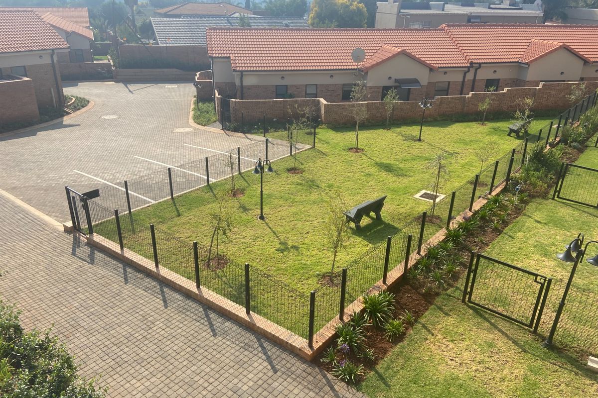 An elevated view of the retirement village grounds, featuring landscaped garden areas, paved walkways, and secure perimeter fencing between residential units.