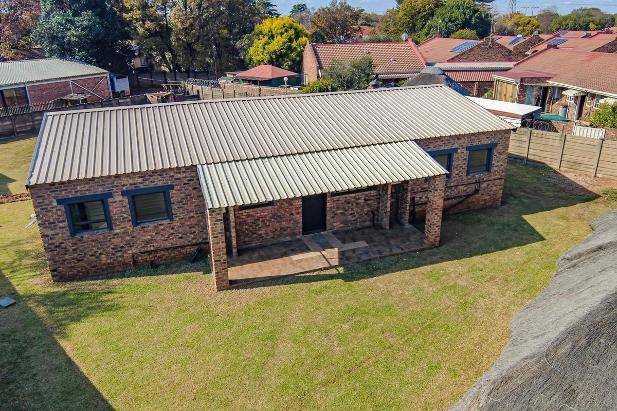 Aerial view of a face brick house featuring a corrugated metal roof and a covered patio area set within a residential garden.
