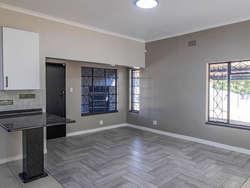 An open-plan living and kitchen area featuring modern herringbone tile flooring, granite breakfast bar, and secure window bars in a neutral color palette.
