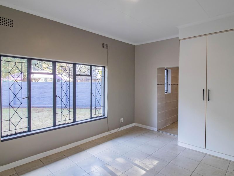 A clean, empty bedroom featuring neutral wall tones, tiled flooring, and a built-in wardrobe with direct access to an adjoining tiled space.