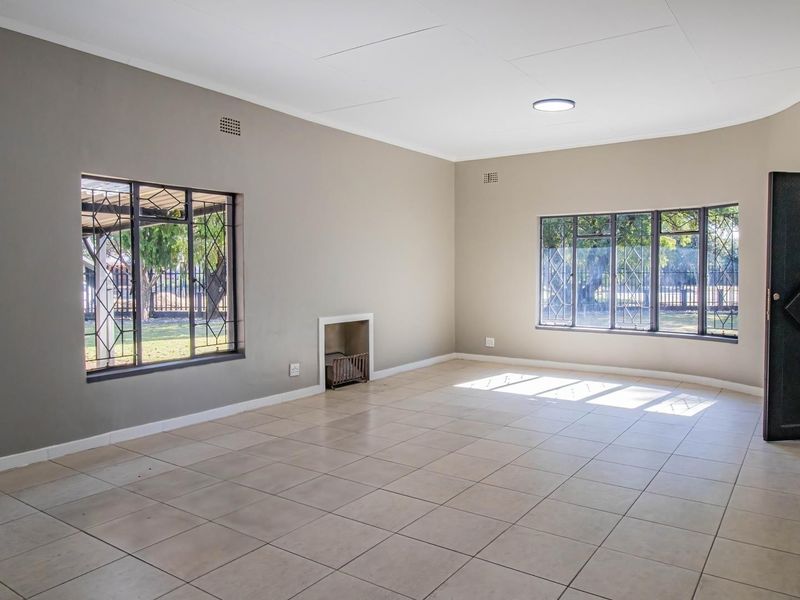 A spacious, empty living room featuring neutral-toned walls, tiled flooring, and a built-in fireplace, offering a versatile blank canvas for interior design.