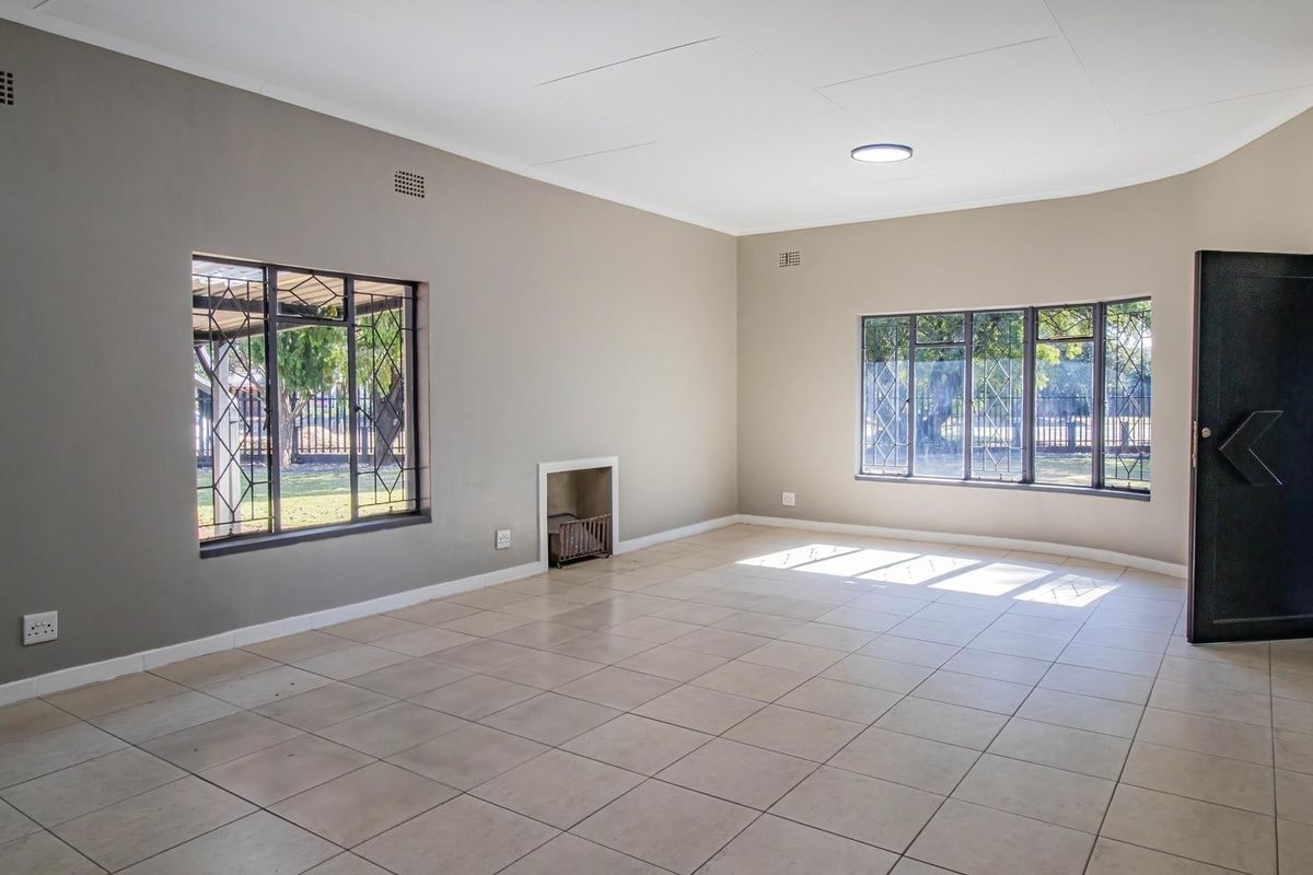 A spacious, empty living room featuring neutral-toned walls, tiled flooring, and a built-in fireplace, offering a versatile blank canvas for interior design.