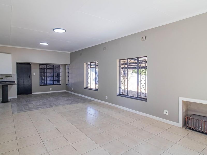 Spacious open-plan living area featuring tiled floors, a built-in fireplace, and an adjoining kitchen space with neutral wall finishes.
