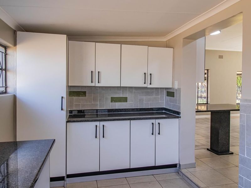 A clean, functional kitchen featuring white cabinetry, dark granite countertops, and a neutral tiled backsplash, opening into an adjacent living area.