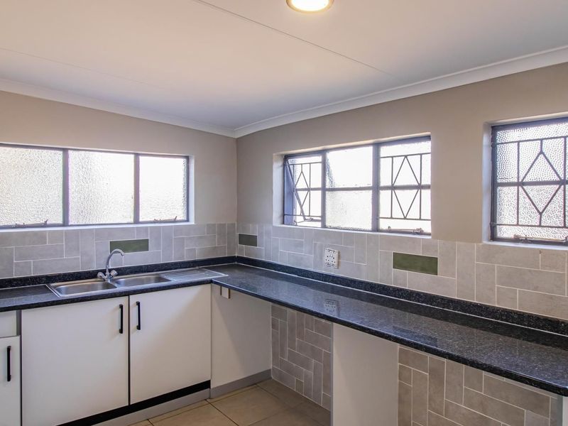 A clean, functional kitchen featuring granite countertops, a stainless steel double sink, tiled backsplash, and ample built-in cabinetry.