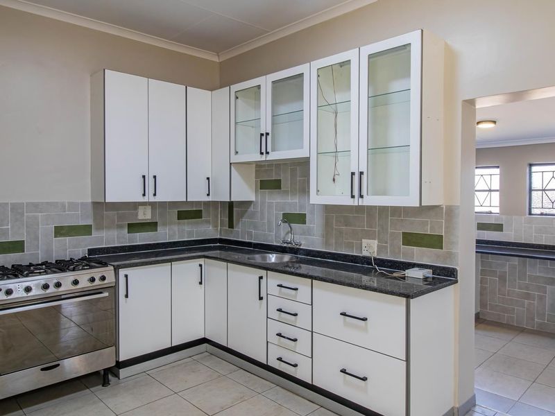 A clean, functional kitchen featuring white cabinetry, granite countertops, a gas stove, and a tiled backsplash, with an adjacent scullery area visible.