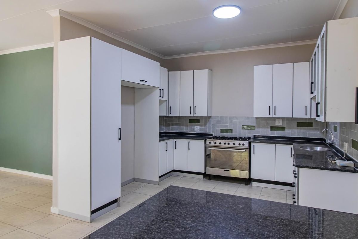 A clean, functional kitchen featuring white cabinetry, dark granite countertops, a gas stove, and tiled flooring, offering a neutral and well-maintained workspace.