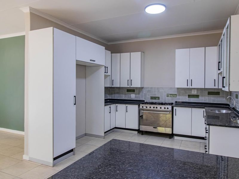A clean, functional kitchen featuring white cabinetry, dark granite countertops, a gas stove, and tiled flooring, offering a neutral and well-maintained workspace.