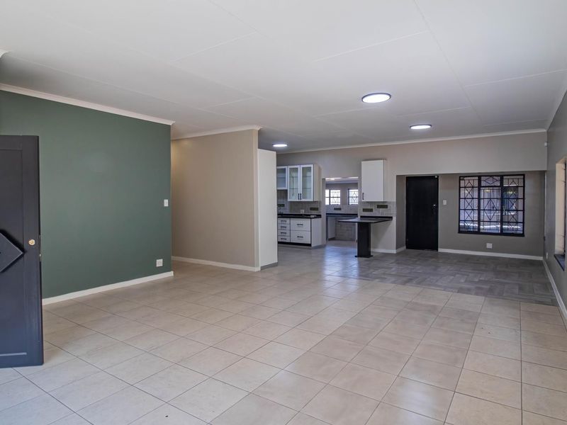 Spacious open-plan living and kitchen area featuring neutral tiled flooring, modern cabinetry, and secure window bars, offering a versatile layout for living and dining.