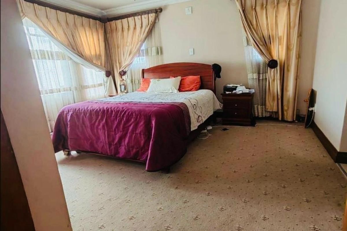 A spacious bedroom featuring wall-to-wall carpeting, crown molding, and large windows with dual-layer curtains.