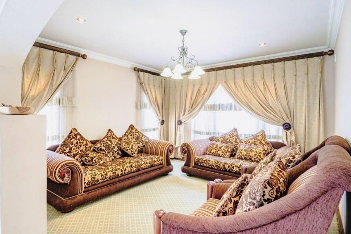 A spacious living room featuring neutral walls, recessed ceiling lighting, and large windows dressed with elegant floor-to-ceiling curtains.