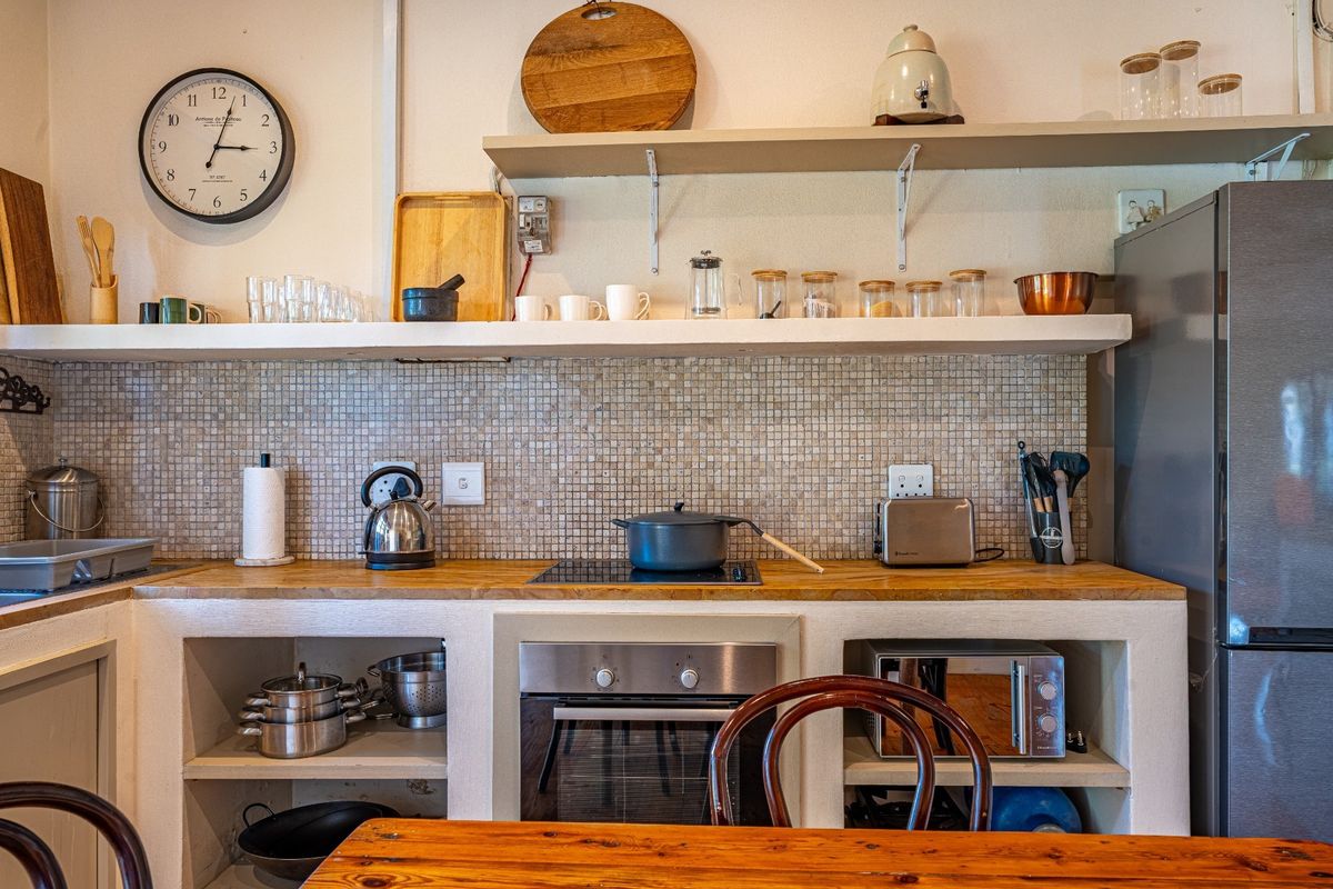 A rustic-style kitchen featuring a mosaic tile backsplash, open shelving, built-in oven, and a wooden countertop with integrated cooktop.