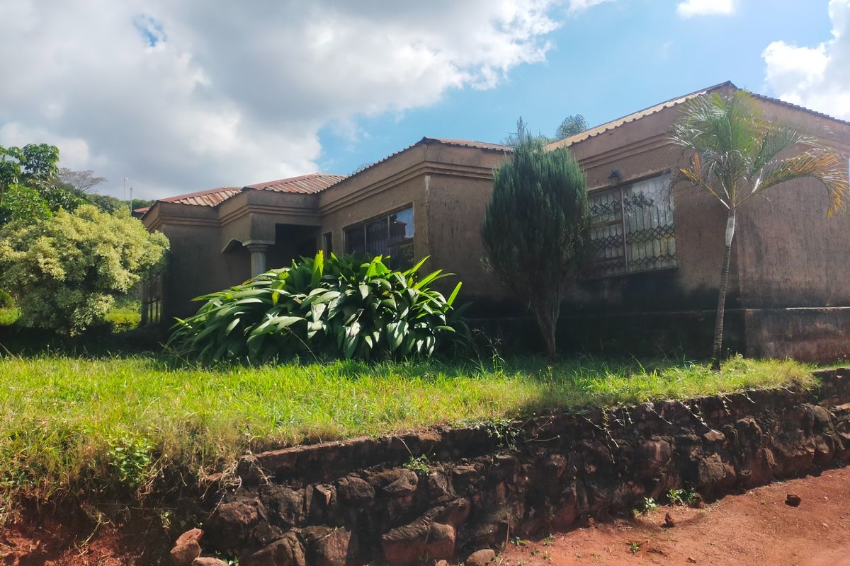 Exterior view of a single-story house featuring a textured facade, metal security window grilles, and a stone retaining wall along the front garden.