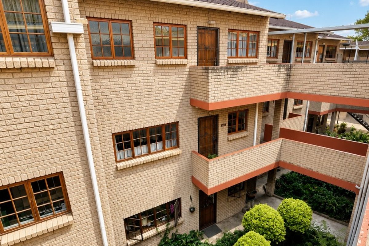 An elevated view of a multi-story retirement village complex featuring face-brick facades, timber-framed windows, and a central landscaped courtyard with walkways.