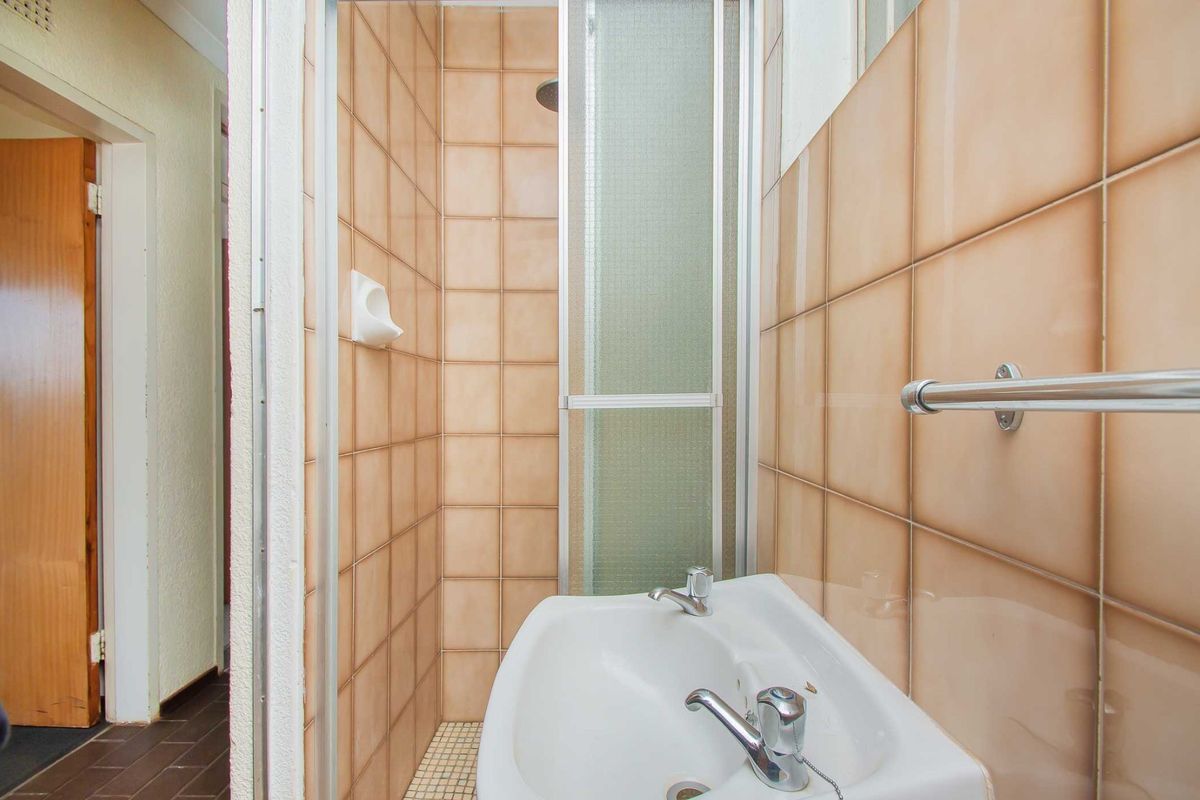 A compact bathroom featuring a shower enclosure with tiled walls and a pedestal washbasin with chrome fixtures.