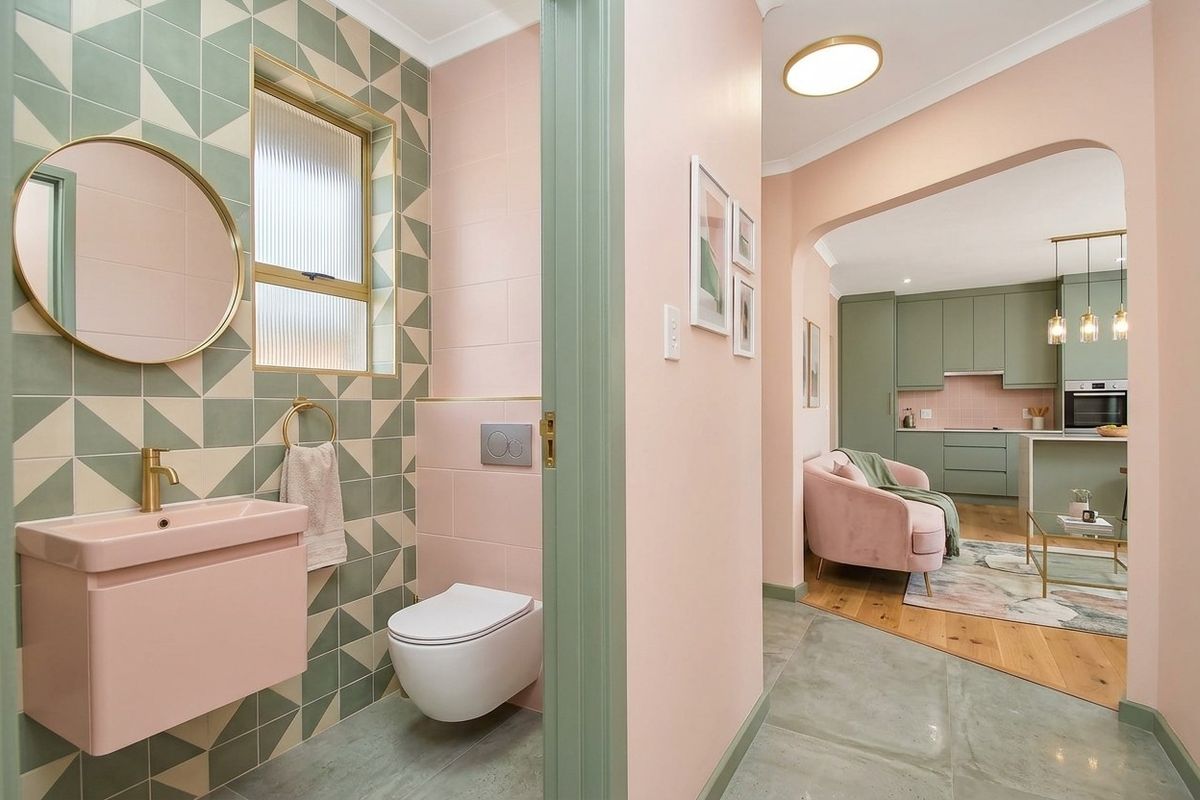A modern, stylish bathroom featuring geometric wall tiles, a wall-hung toilet with concealed cistern, and a pink wall-mounted vanity with brass fixtures.
