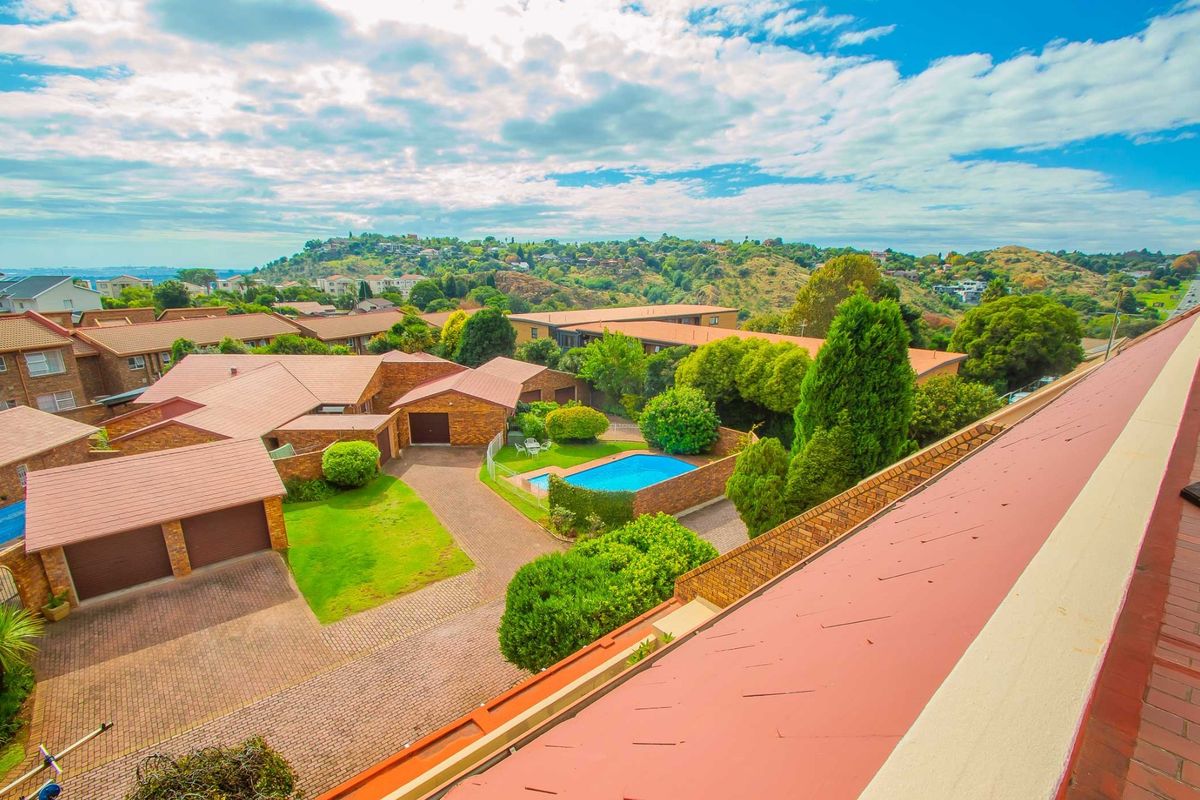 Elevated aerial view of the residential complex featuring a swimming pool, paved driveways, and surrounding landscaped gardens with scenic hillside views.
