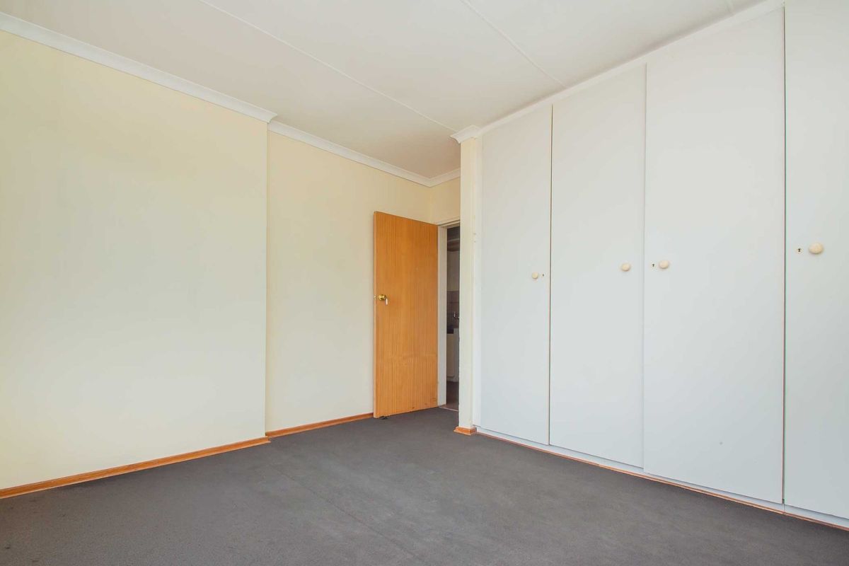 A clean, empty bedroom featuring neutral walls, carpet flooring, and ample built-in cupboard storage space.