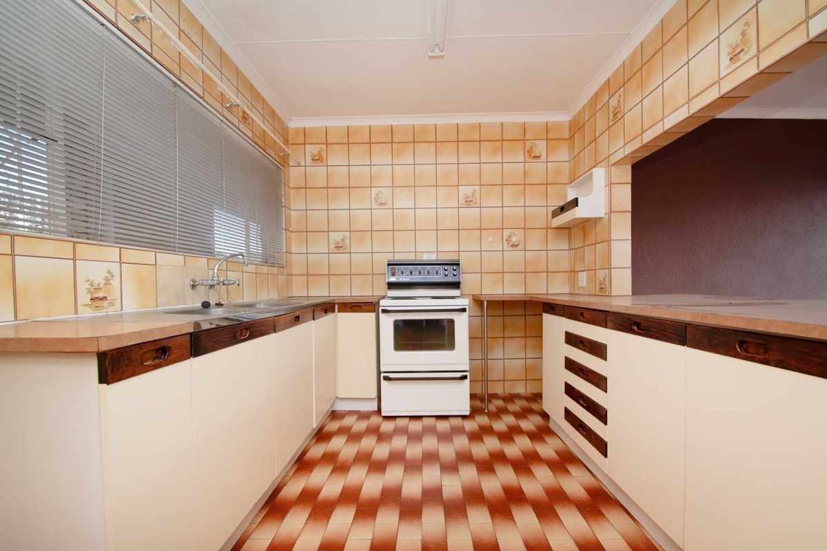 A dated kitchen featuring original cabinetry, laminate countertops, and ceramic tiling throughout, offering a functional layout ready for modern renovation.