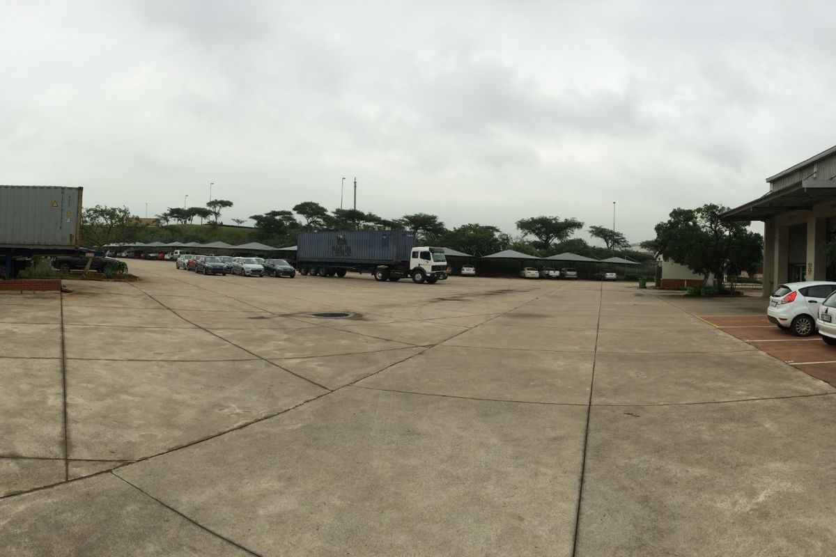 A wide-angle view of an industrial yard featuring extensive concrete hardstanding, parking bays, and access to warehouse facilities.